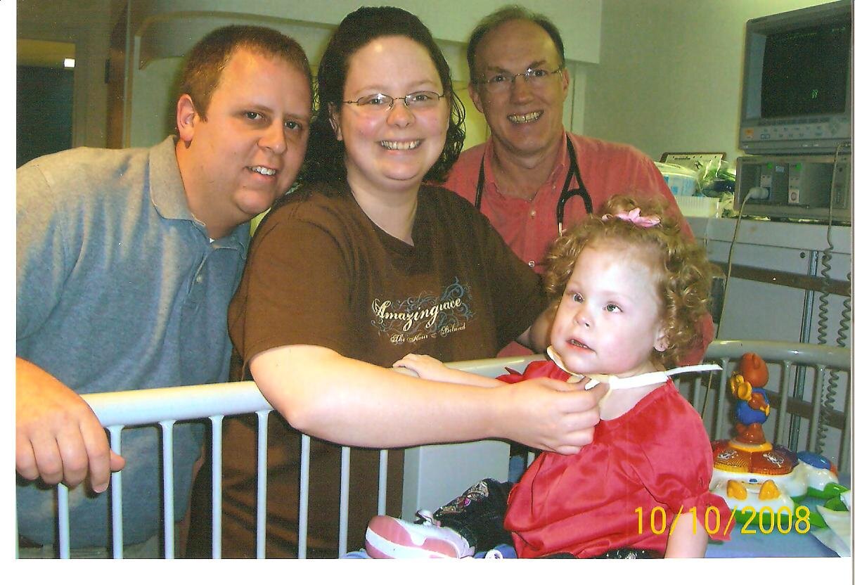 Nathan and Dr. Makris watch Kim remove the trach from two-year-old Emily, who had undergone trach surgery two years earlier. 